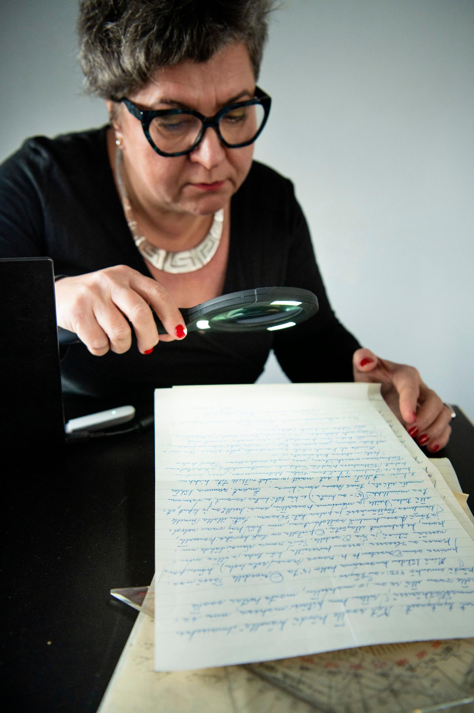 Anna Hurmalainen tutkii käsialaa suurennuslasilla.