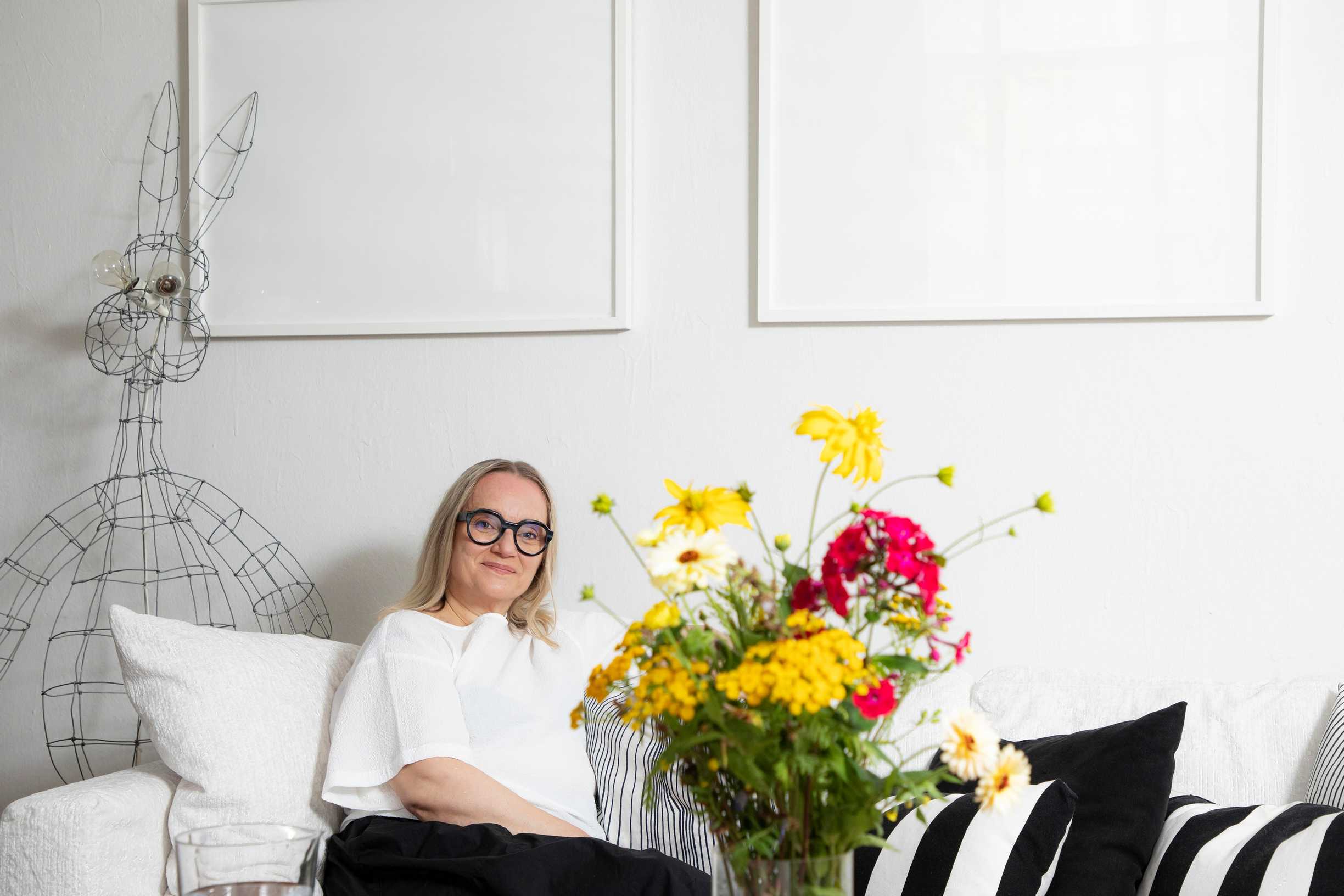 Helena Hietanen istuu sohvalla, etualalla kukkakimppu