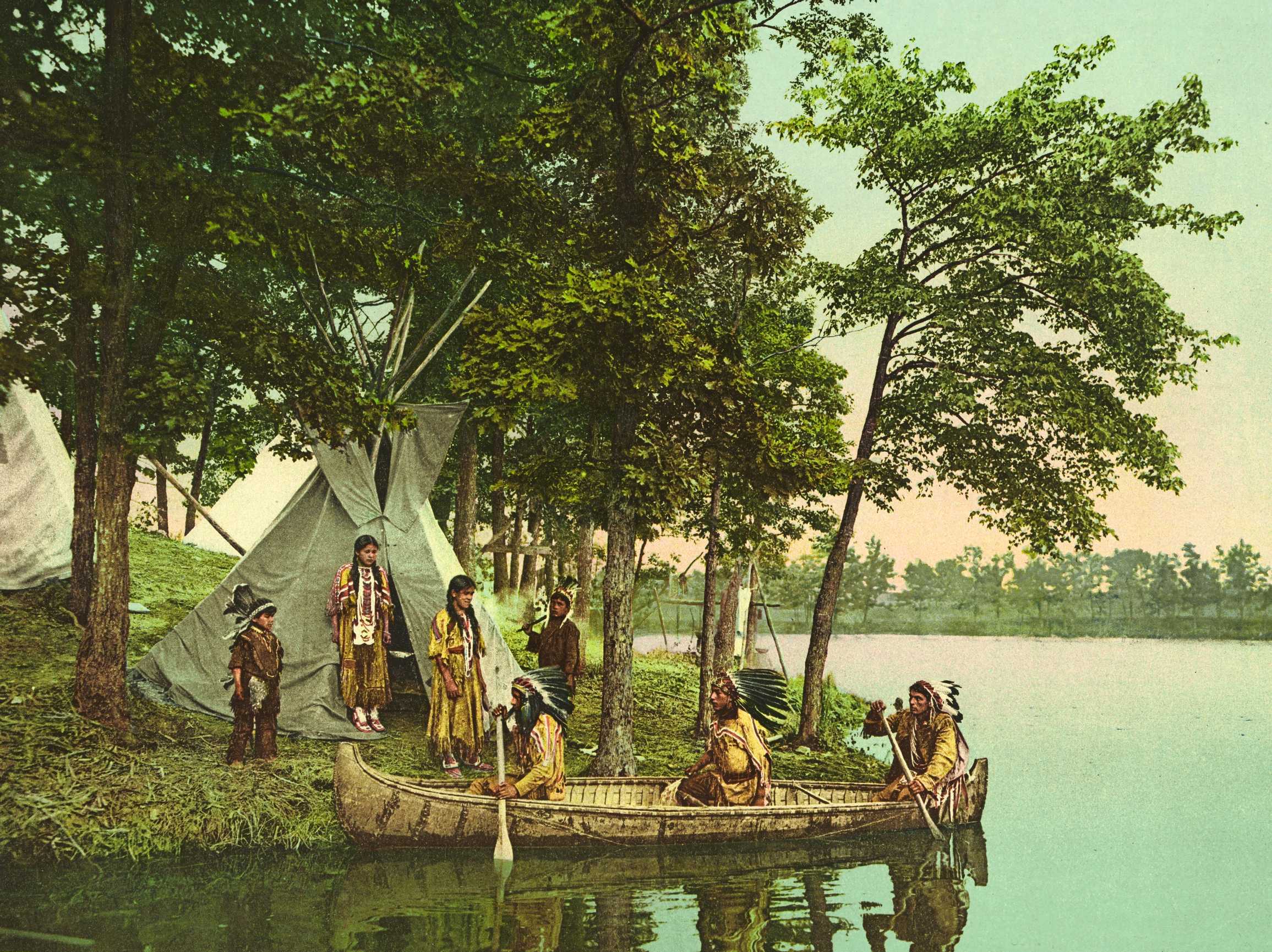 Pohjois-Amerikan alkuperäiskansaa melomassa kanootilla joella, taustalla tiipii.